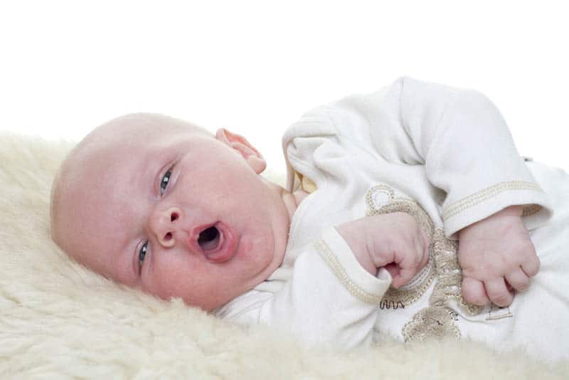 cute baby lying on a sheepskin and coughing