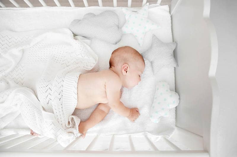 cute baby sleeping in a crib coveres with white blanket