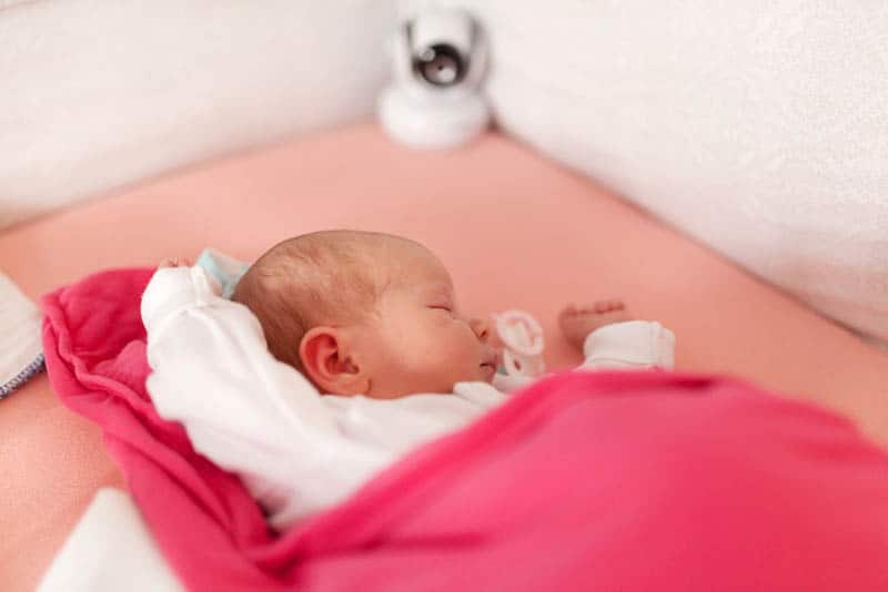 cute baby sleeping in a crib with cam monitor in the crib corner