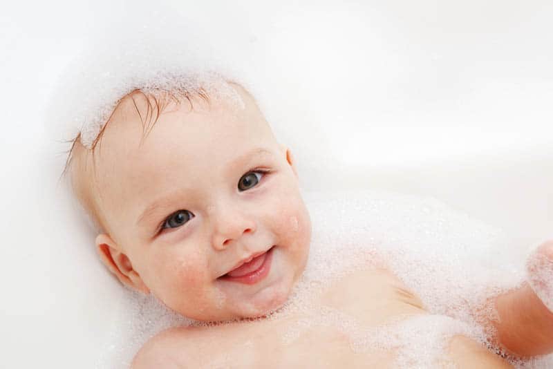 cute baby smiling while taking bath covered with foam
