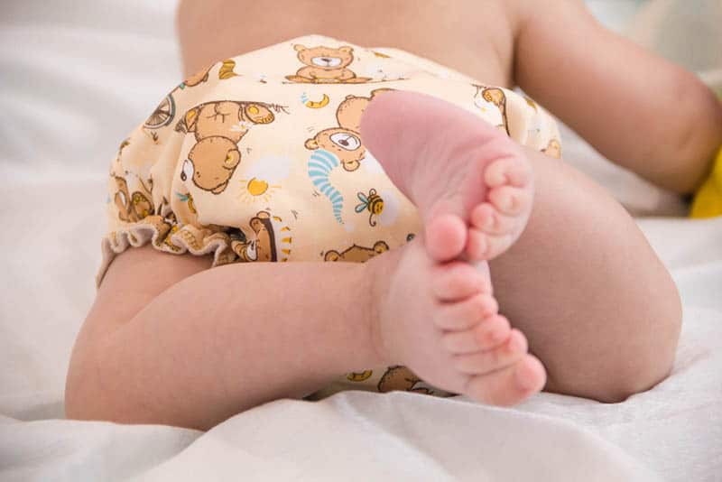 cute baby wearing cloth diapers lying on tummy in white sheet
