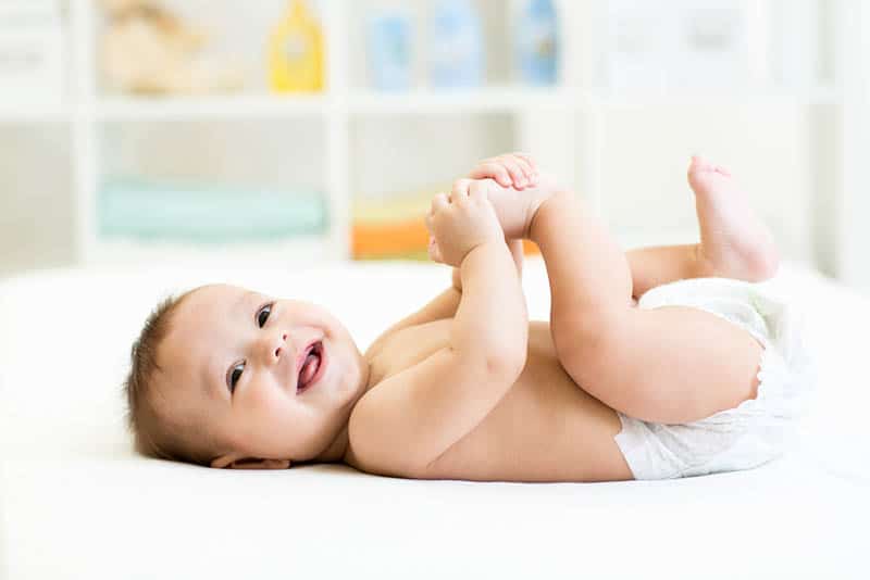 cute baby wearing diapers lying on bed and smiling