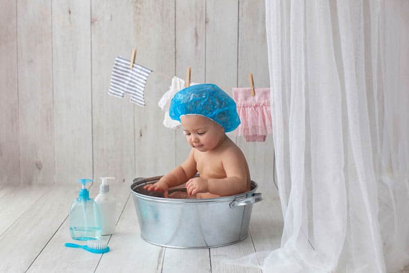 cute baby with blue shower cap taking a bath in a bassinet