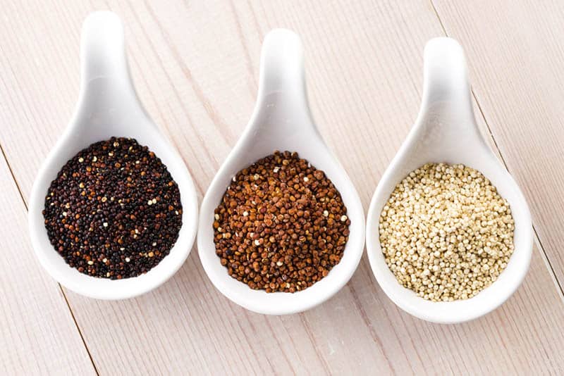different types of quinoa grain in three white spoon bowles on the wooden table