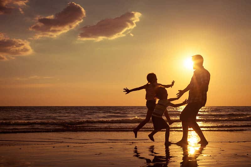 father playing with his kids on the beach at sunset