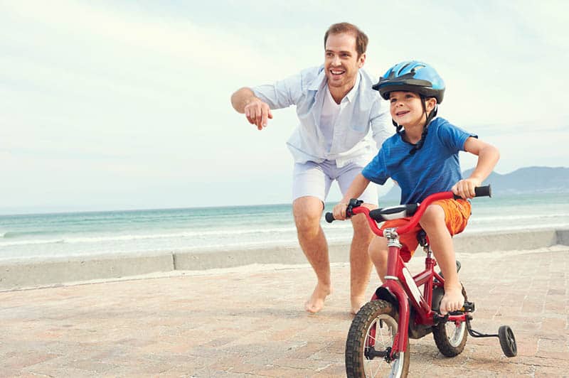 father teaching son to ride a bike near the beach