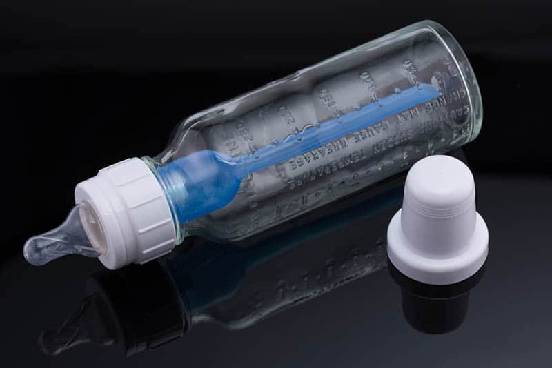 glass baby bottle with white plug on the dark table 