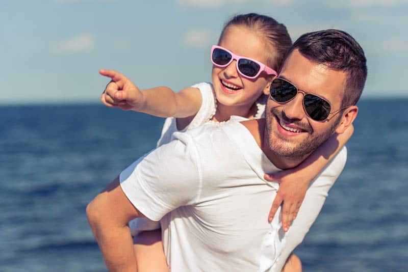 handsome father carrying his daughter on back wearing sunglasses both of them