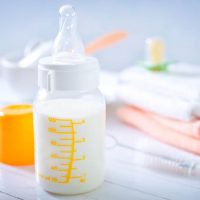 a baby bottle filled with milk in front of folded baby clothes