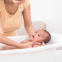young mother bathing cute baby in a plastic baby bathtub