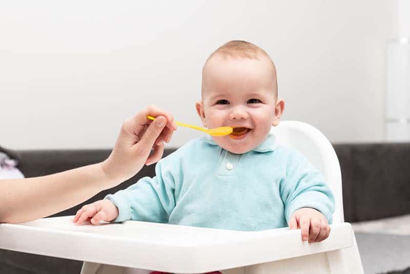 mother feeding her happy baby in a high chair at home