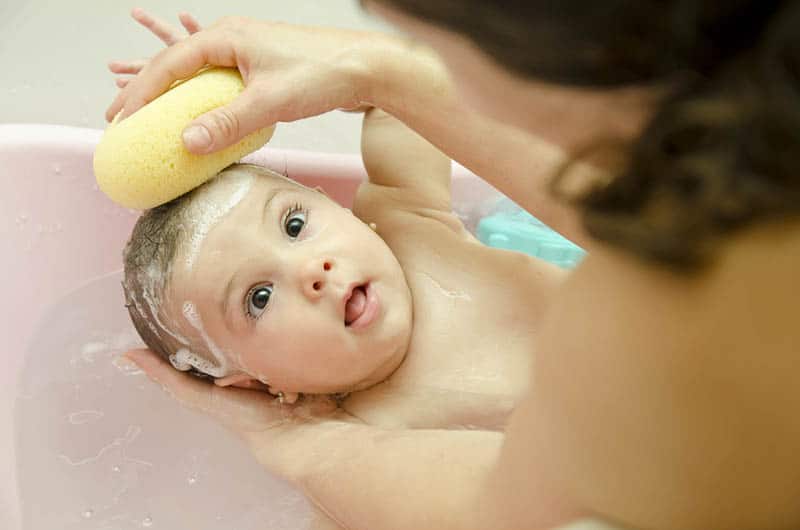 mother washing baby hair with yellow sponge and a shampoo