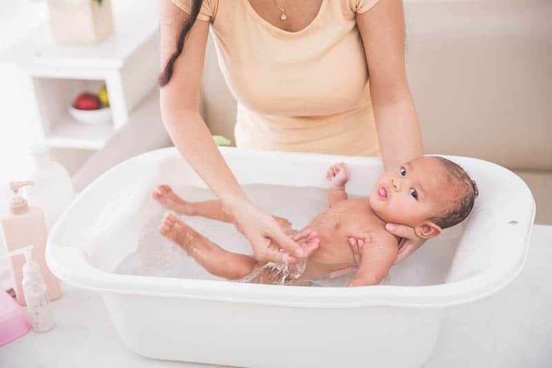 mother washing her baby in a white shower bassinet in bathroom