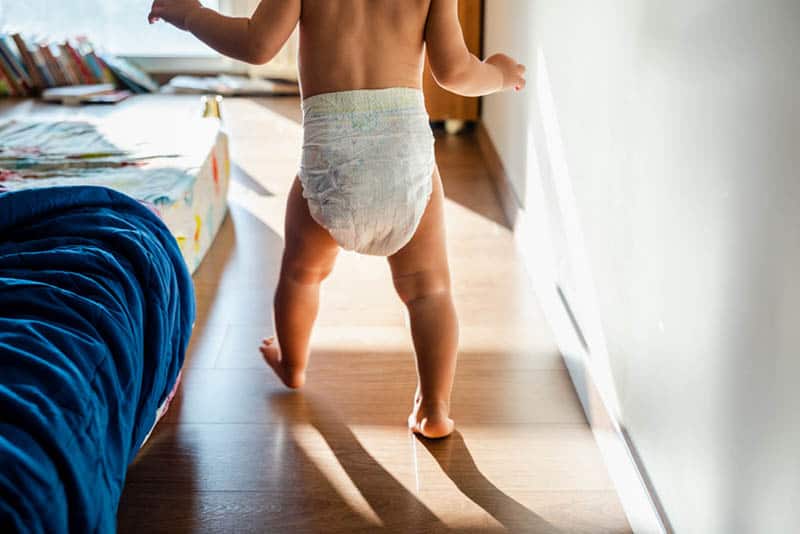 naked baby wearing diapers walking in the bedroom