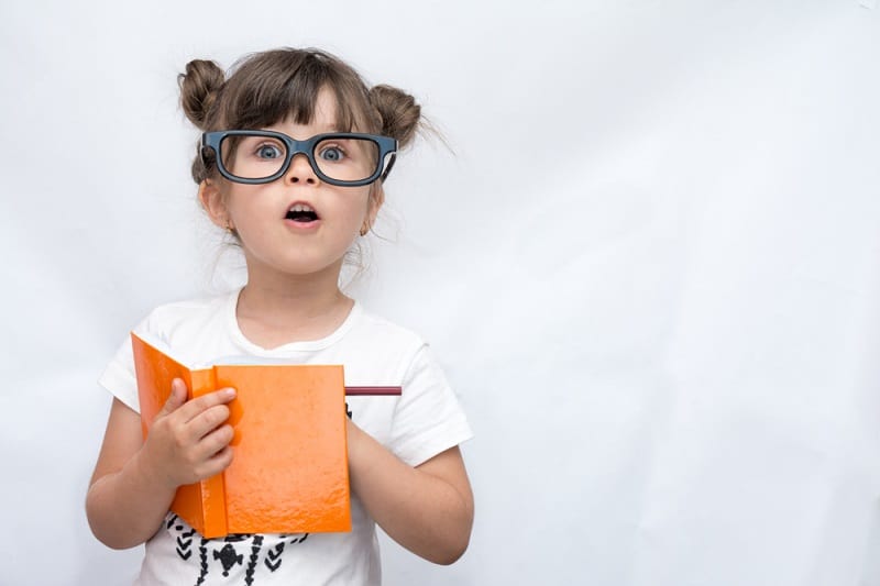 nerdy little girl wearing big glasses and writing in a notebook