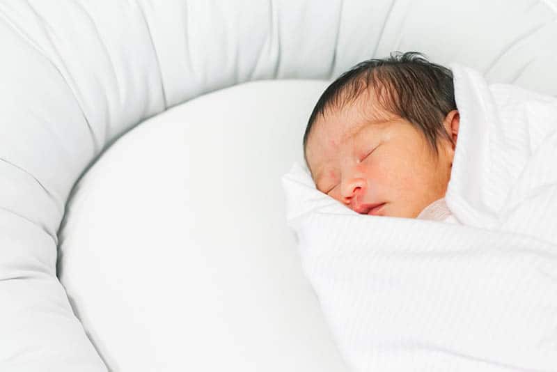 newborn baby sleeping in a white baby nest wrapped into blanket