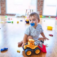 cute baby boy with pacifier sitting on the floor with toys