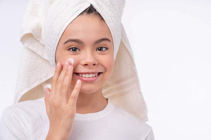 pretty smiling girl with hair in towel using face cream
