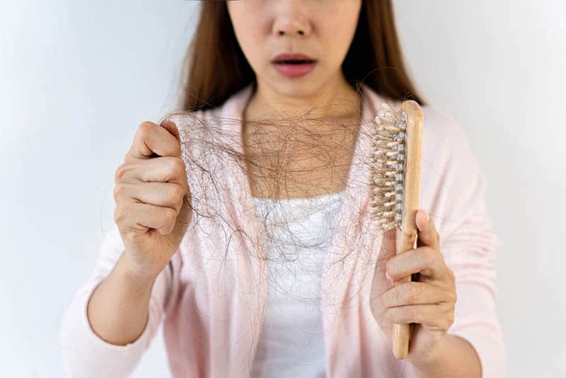 shocked pregnant woman looking at hair loss in her hand with brush