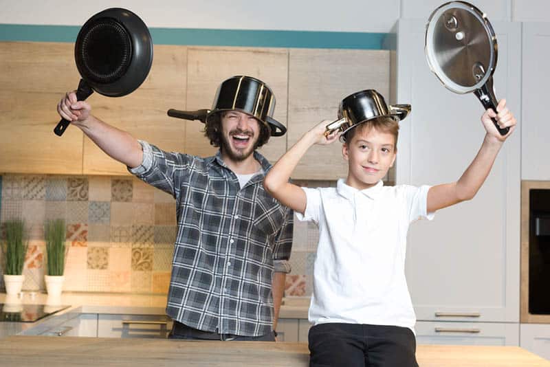 silly father and son playing with kitchen dishes at home