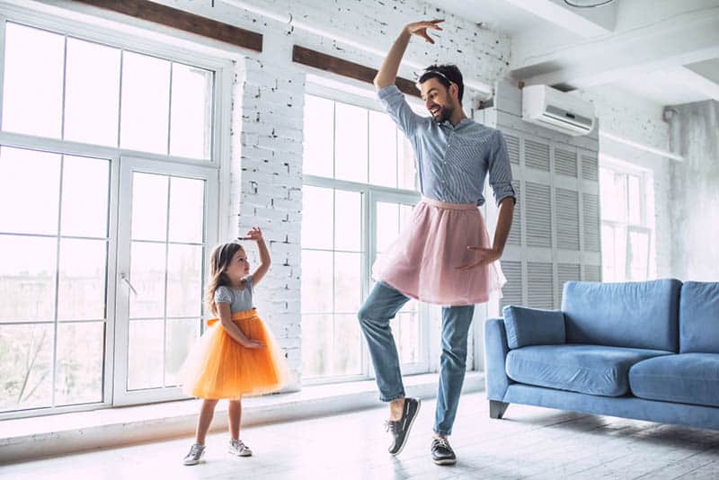 silly father dancing with his cute little daughter in skirts