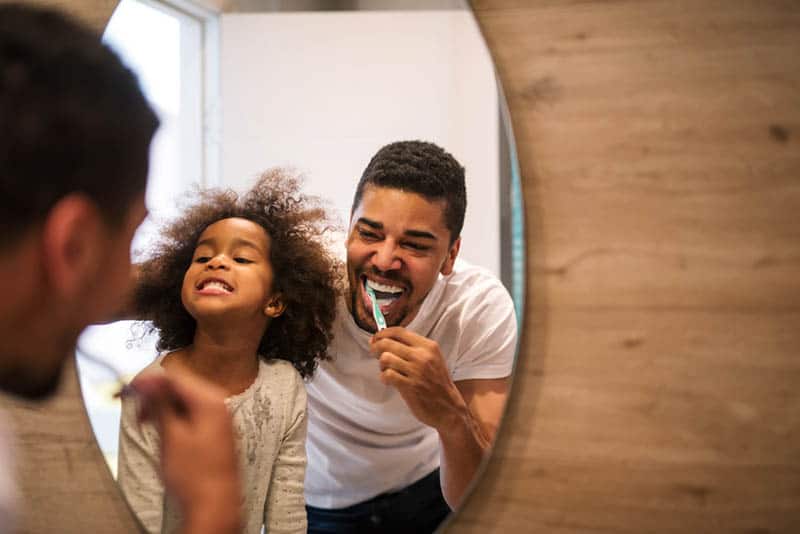 smiling father brushing his teeths with daughter in the bathroom
