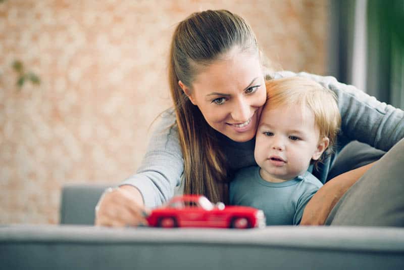 smiling mother playing with her son with red car toy at home
