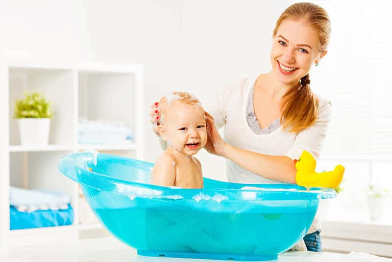 smiling mother posing with happy baby in bathtube at home