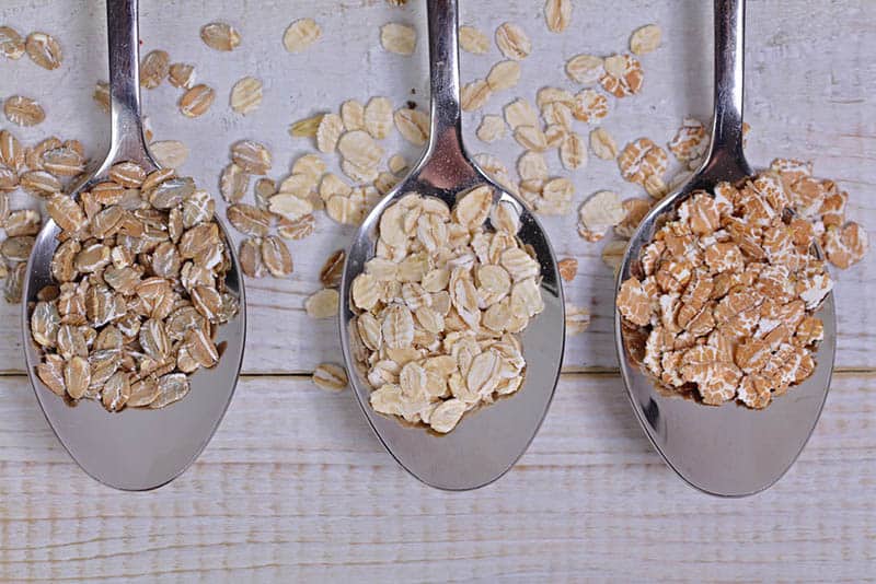 three kitchen spoons with whole grain oats on the wooden table