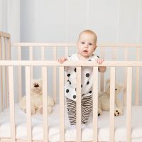 cute baby girl standing in the crib while holding the rails