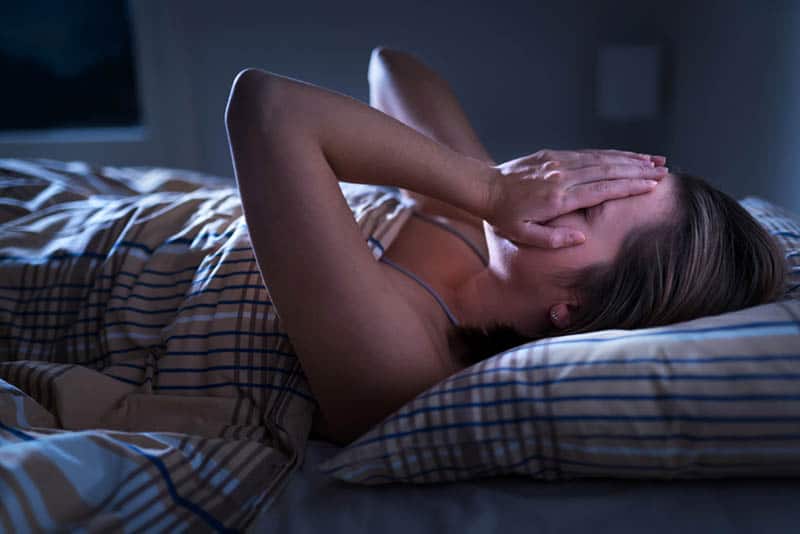 woman covering face with hands while having a nightmare in bed