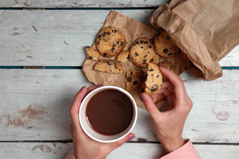 woman holding a cup of coffee and a bag full of cookies on the wooden table