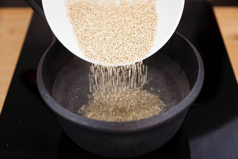 woman putting whole grain quinoa to the boiling water
