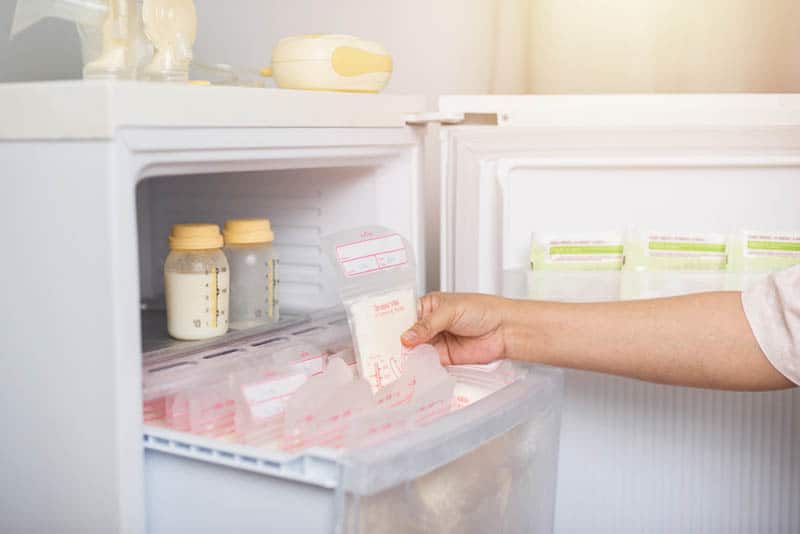 woman taking breast milk frozen in plastic storage bags in refrigerator