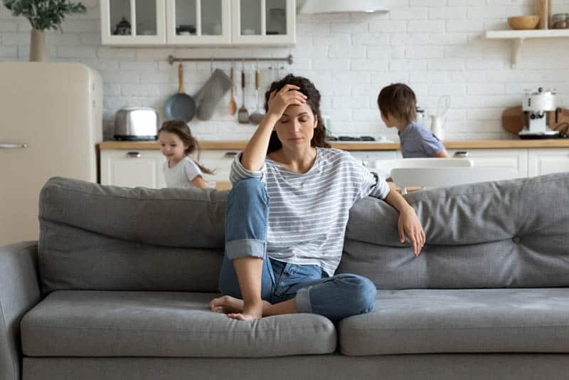 worried mother sitting on the couch while kids running around