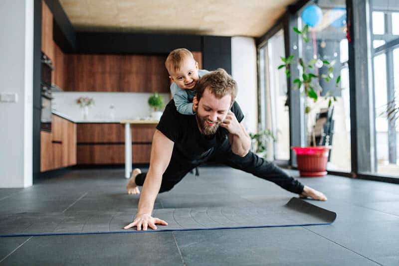 young father exercising at home while carrying his son on back