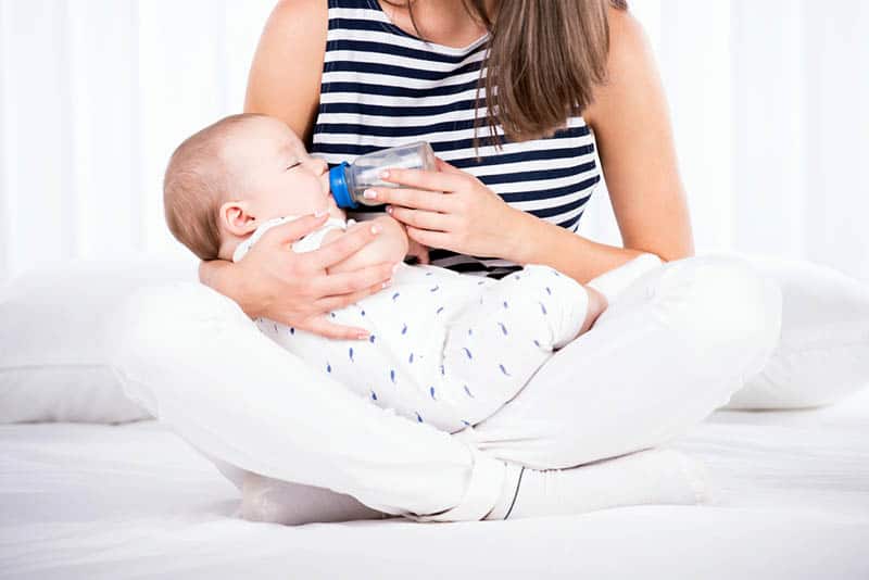 young mother feeding her baby with milk bottle in a lotus position