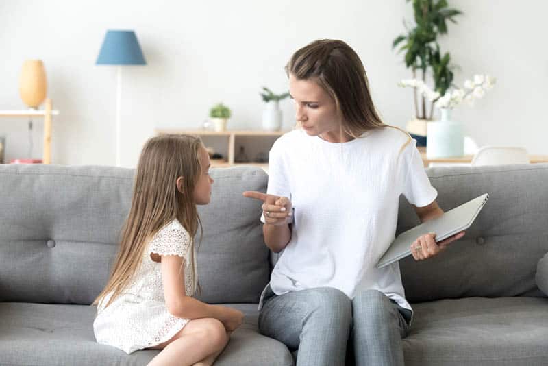 young mother talking to daughter on the couch while holding laptop
