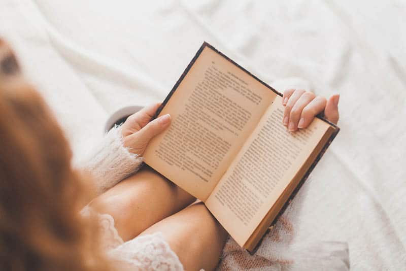 young woman in a sleeping dress reading a book in the bed