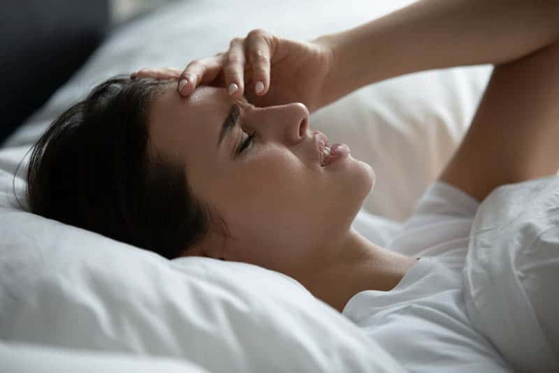 young worried woman lying in bed holding for head