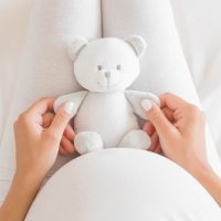 pregnant woman holding a teddy bear toy for her unborn baby in her lap