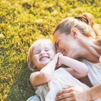 single mom and daughter laughing while laying on the grass