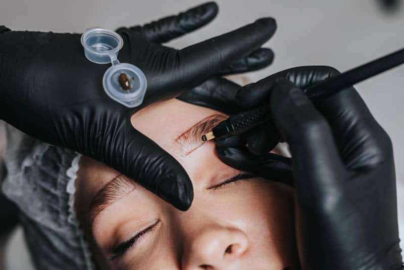 Cosmetologist preparing young woman for eyebrow permanent makeup