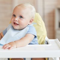 baby wearing a burp cloth sits in a high chair