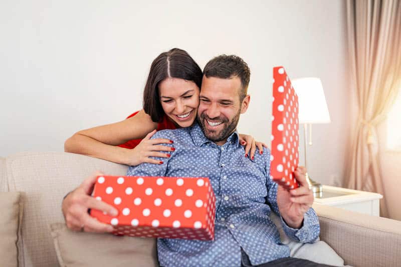 Woman surprising her husband with a gift on the couch