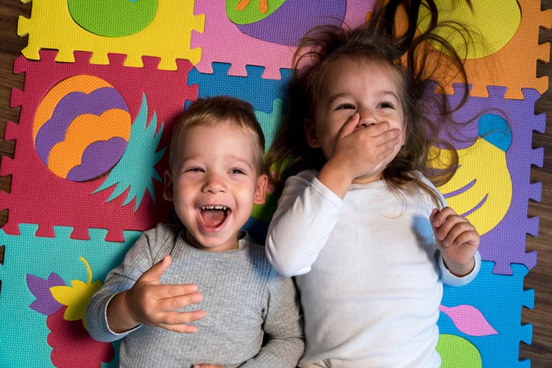 adorable baby boy laughing with sister on a playing mat