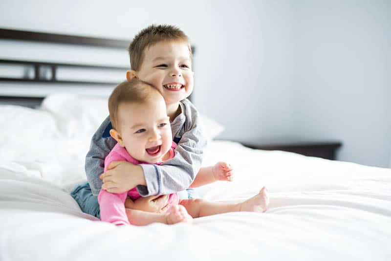 adorable little kid hugging his baby sister on the bed