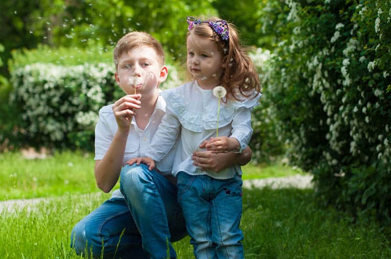 brother and little sister playing with dandelions in the garden