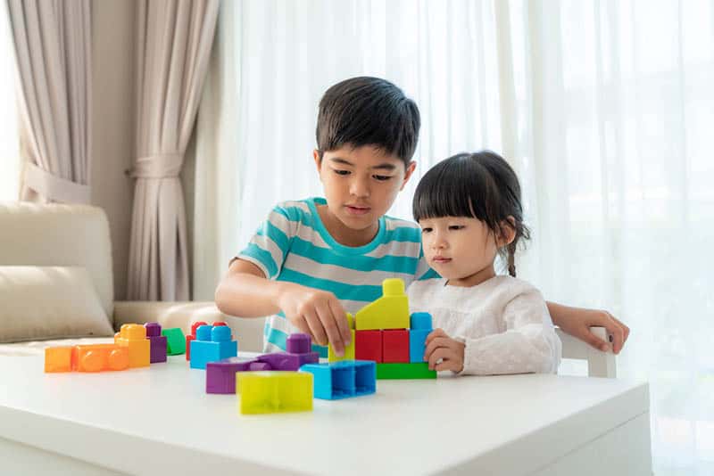 brother and sister playing with cubes on the table at home
