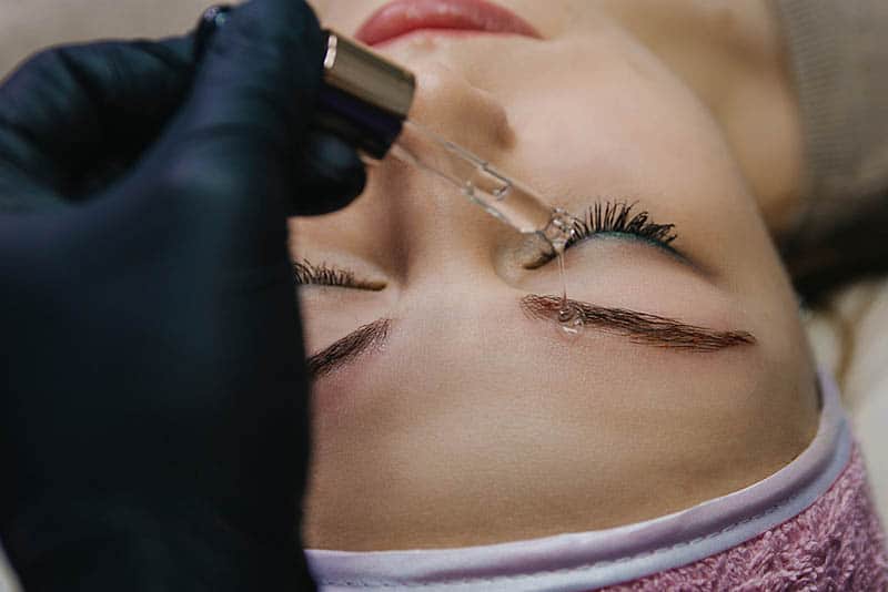 cosmetologist using liquid on woman's eyebrow after microblading